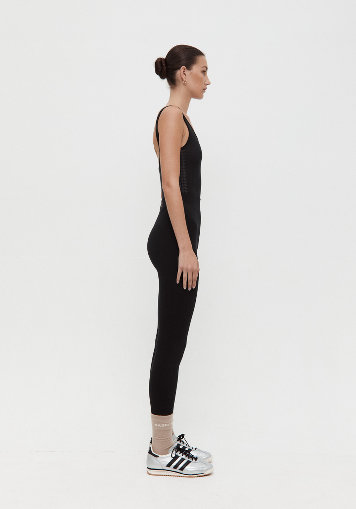 Person wearing a black sleeveless top and leggings with Adidas shoes on a white background