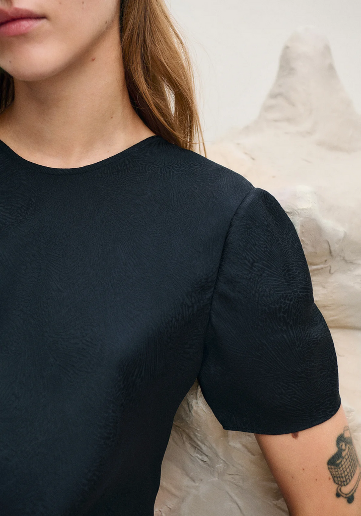 Person wearing a black dress with short sleeves against a neutral background