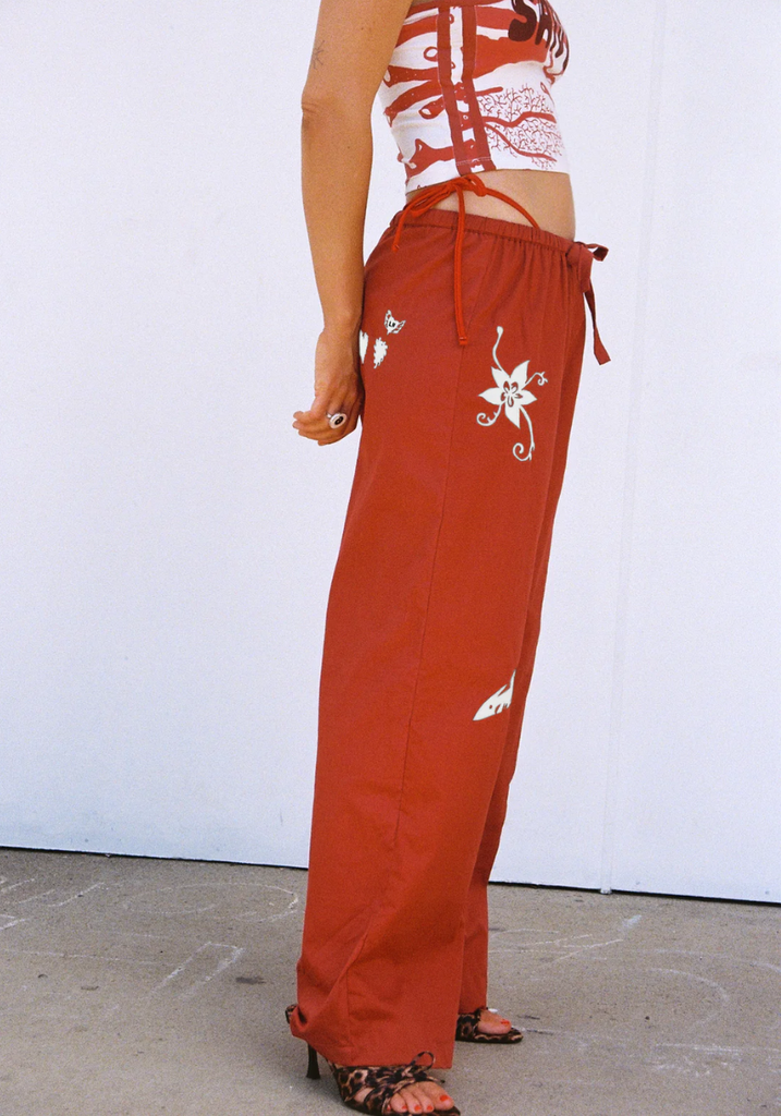 Person wearing red pants with white floral embroidery on a plain background