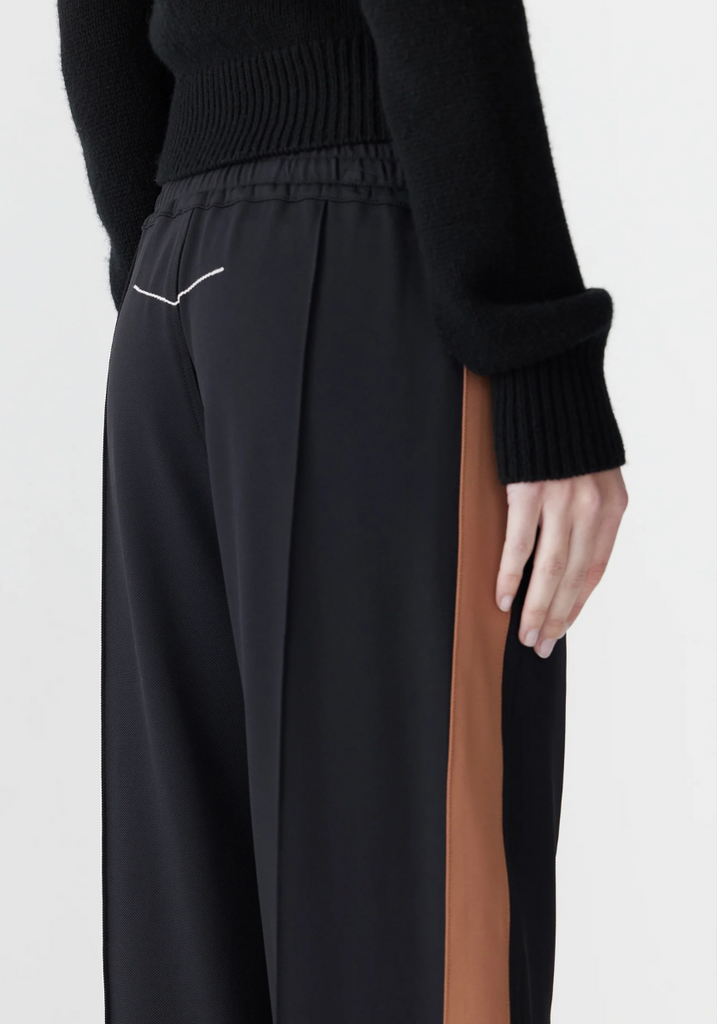 Black pants with a brown stripe worn by a person on a white background