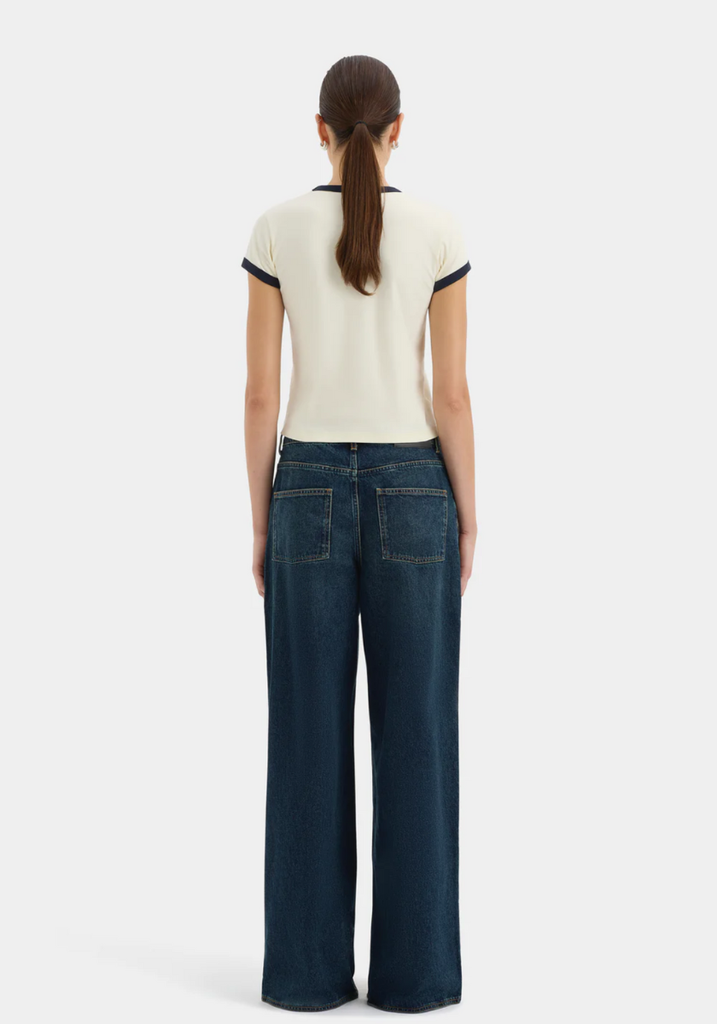 Person wearing a white top with black trim and dark blue jeans on a white background