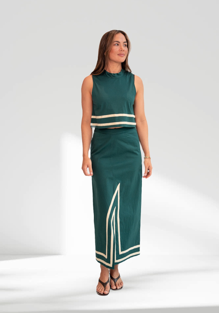 Woman wearing a green sleeveless top and long skirt with white trim on a white background